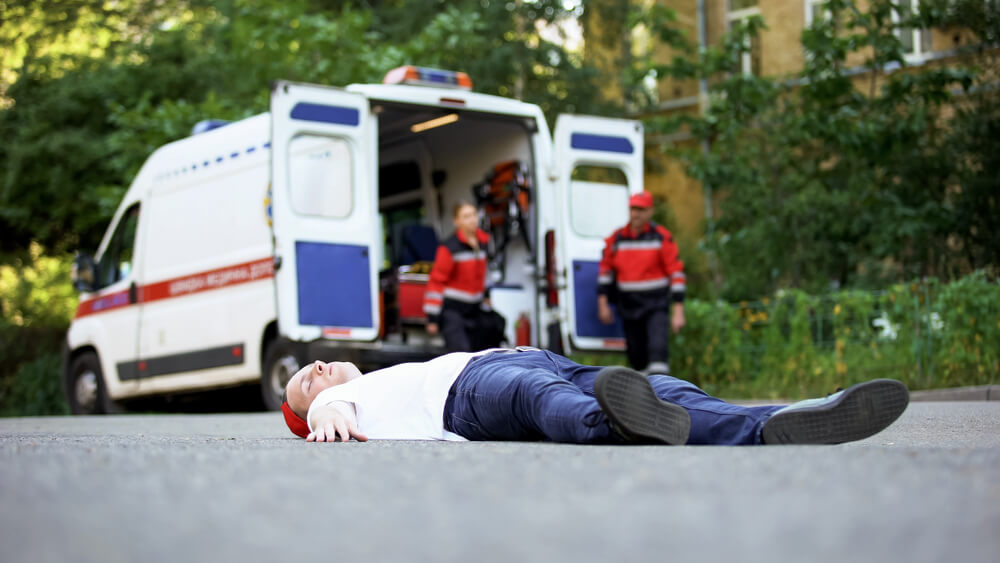 A person lies unconscious on the ground in front of an ambulance