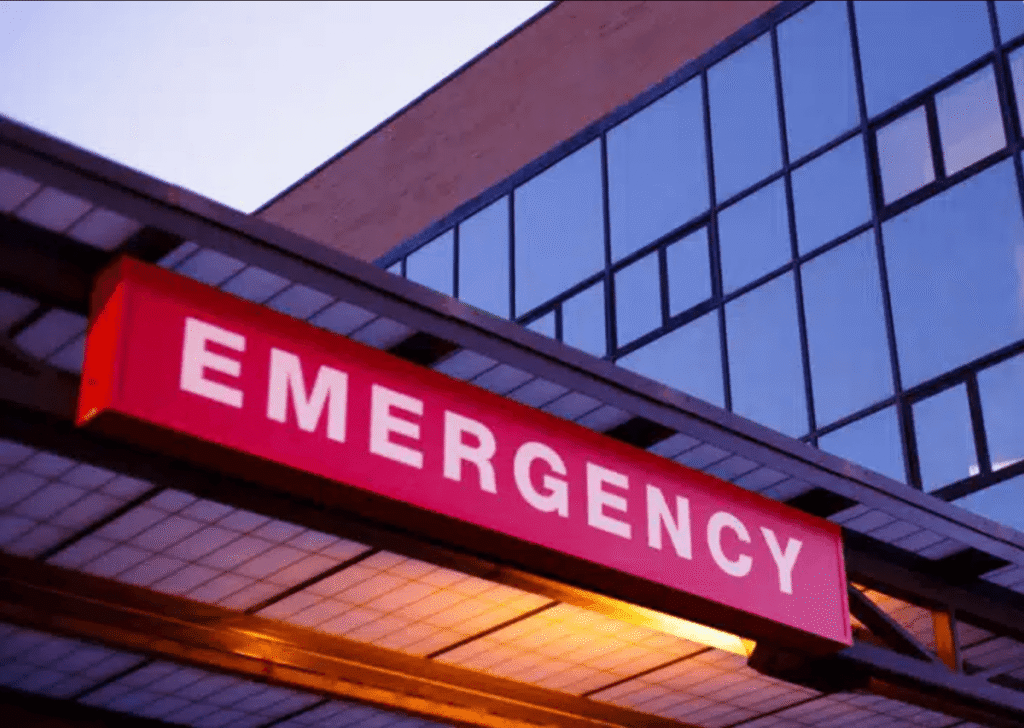 red "EMERGENCY" sign illuminated above the entrance of a hospital