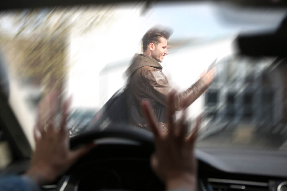blurred motion scene from inside a car shows a driver’s hands raised in panic as a pedestrian