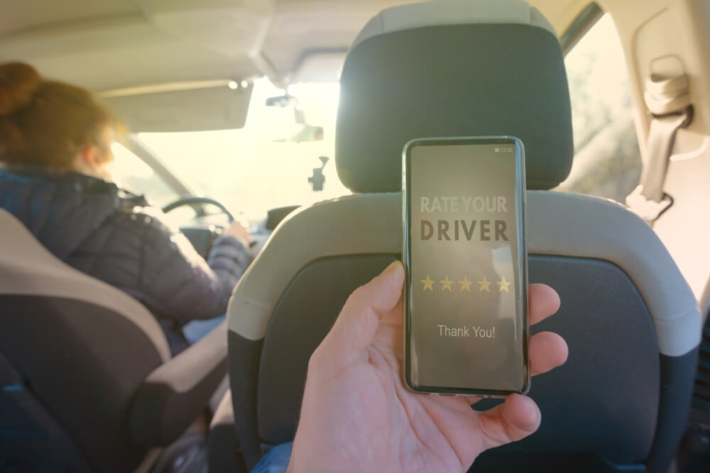 passenger in the backseat holding a smartphone displaying a five-star driver rating