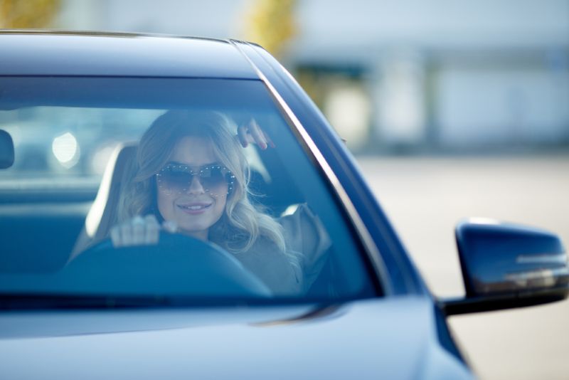 blonde woman in sunglasses driving a sedan