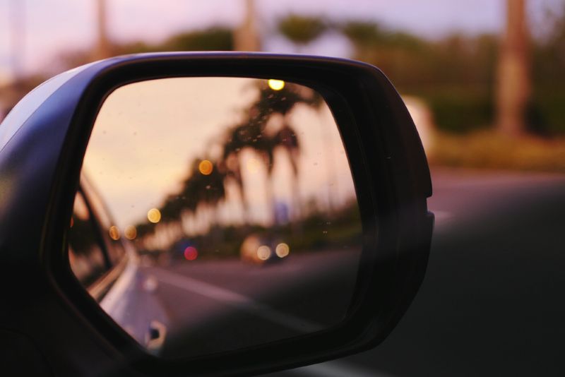 view out the side mirror of a car driving at sunset