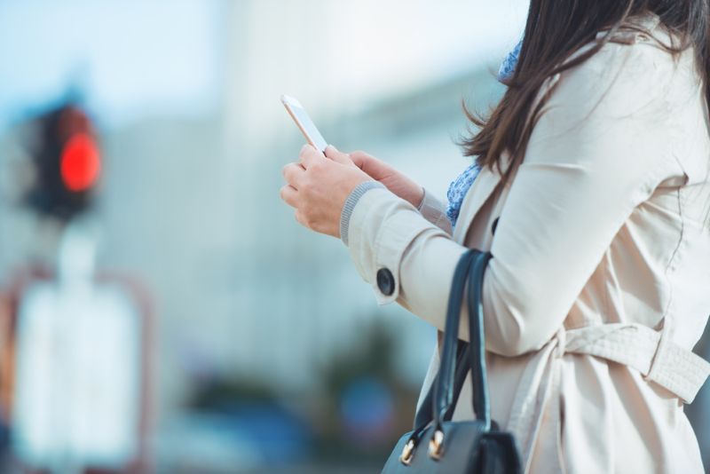 Woman in a trench coat using her phone while crossing the street