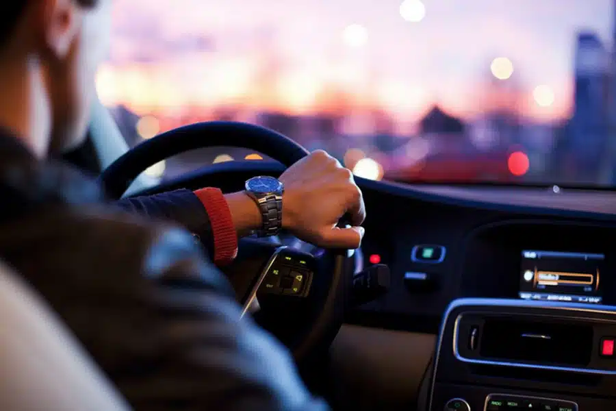 driver wearing a leather jacket and a wristwatch grips the steering wheel of a car