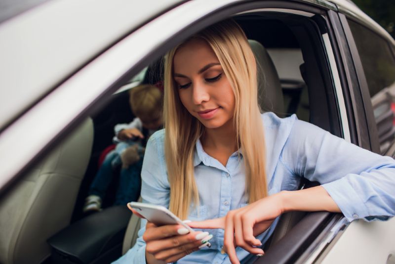 Woman scrolling her phone with child in back of car